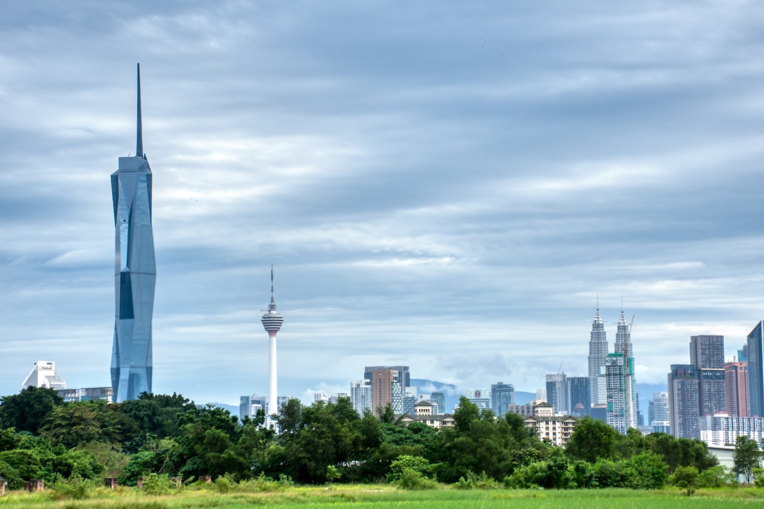 Merdeka 118 and the KL Tower rising beyond open green land on the edge of Kuala Lumpur